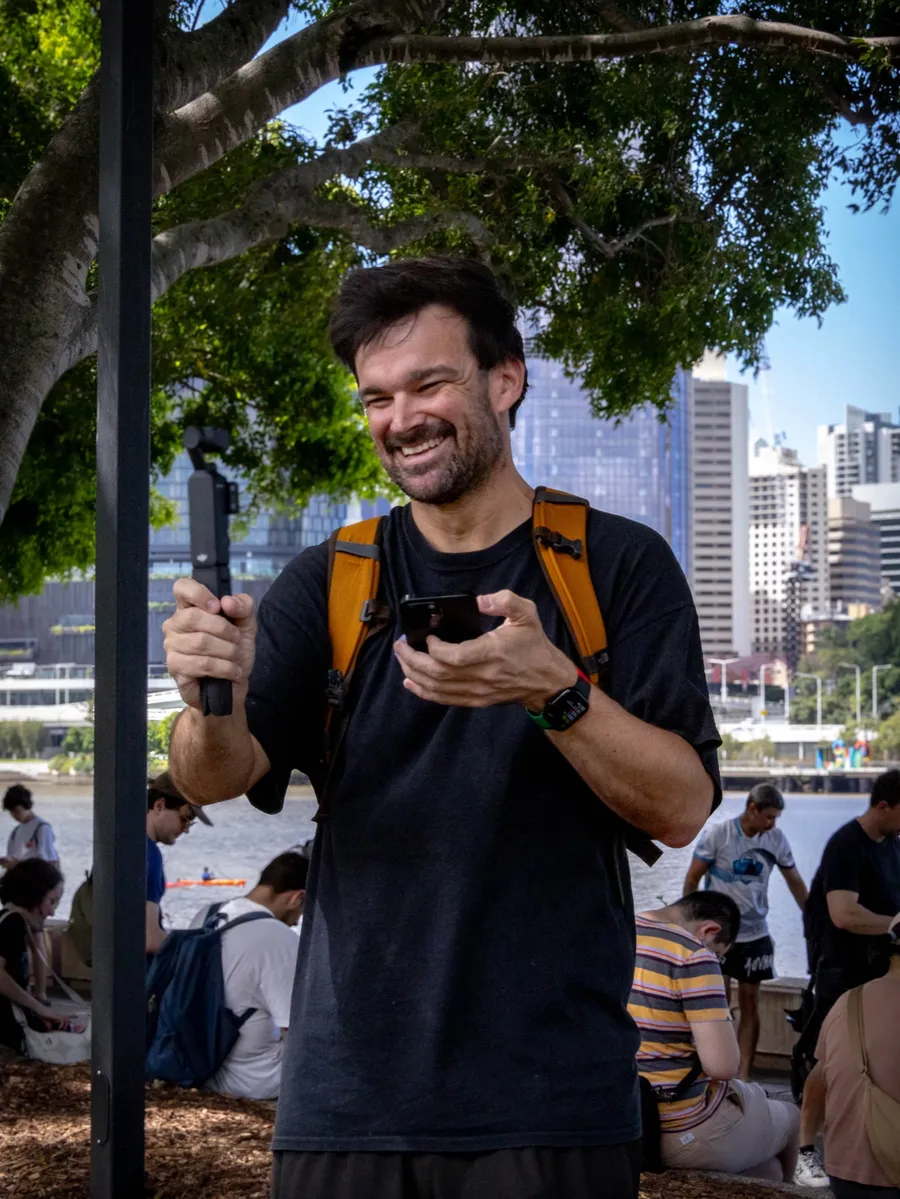 Matt filming on his phone by the Brisbane River